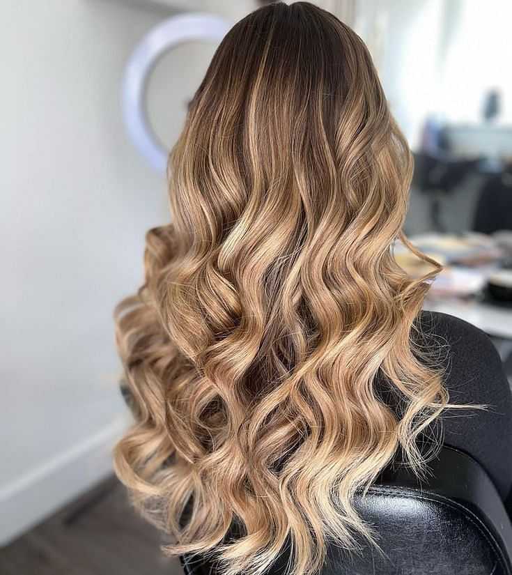 Woman with long, wavy, blonde and brown ombre hair sitting in a salon chair.