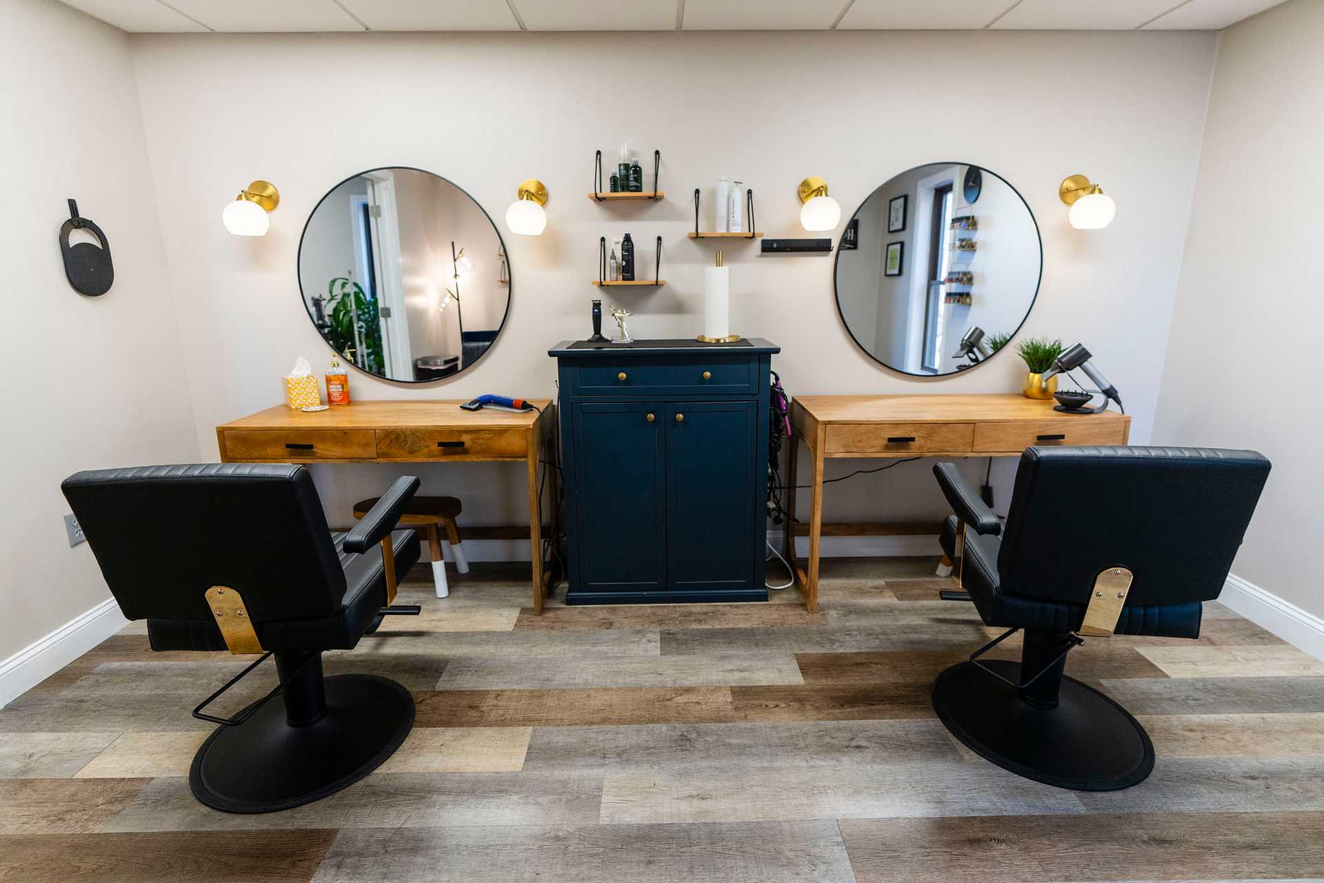 Barber shop interior with two chairs, wooden counters, round mirrors, and modern lighting.