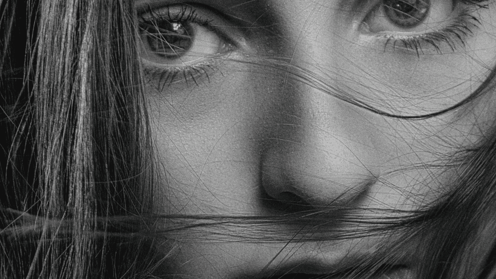 Close-up black and white photo of a person's intense eyes, with hair partially covering their face.